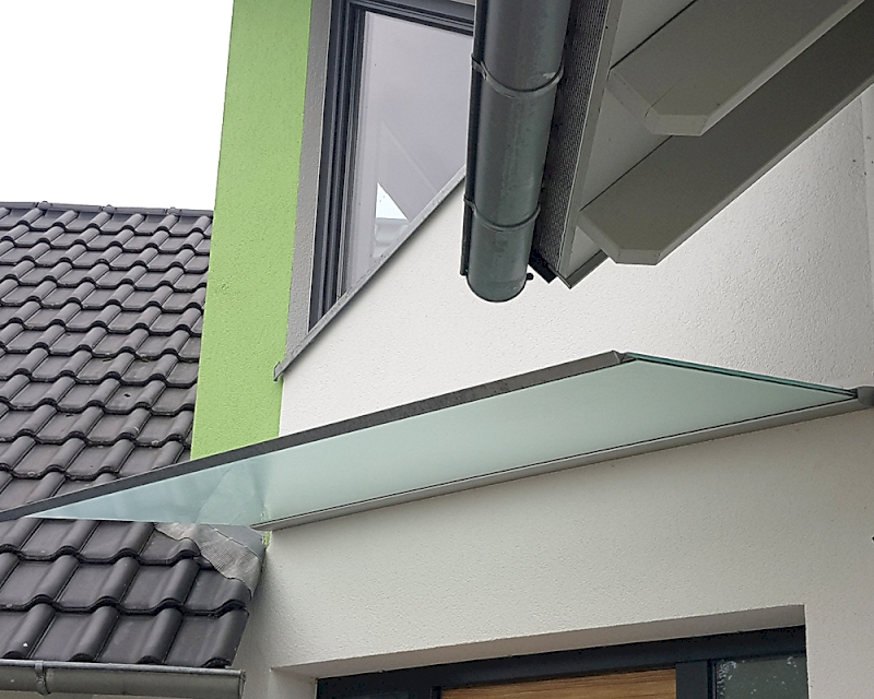 Vordach aus VSG Glas mit mattierter Folie und freihängendes Vordachsystem